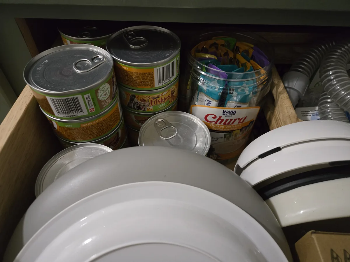 Our cat treat drawer — Friskies wet food, Churu jar, lick plates stacked and ready to go