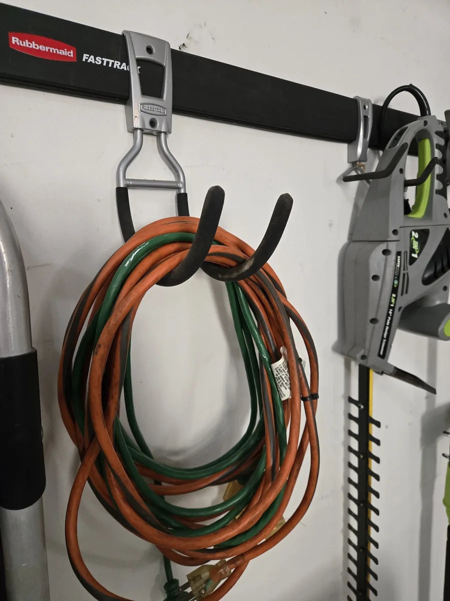 Extension cords and garden hose on utility hooks, with hedge trimmer above