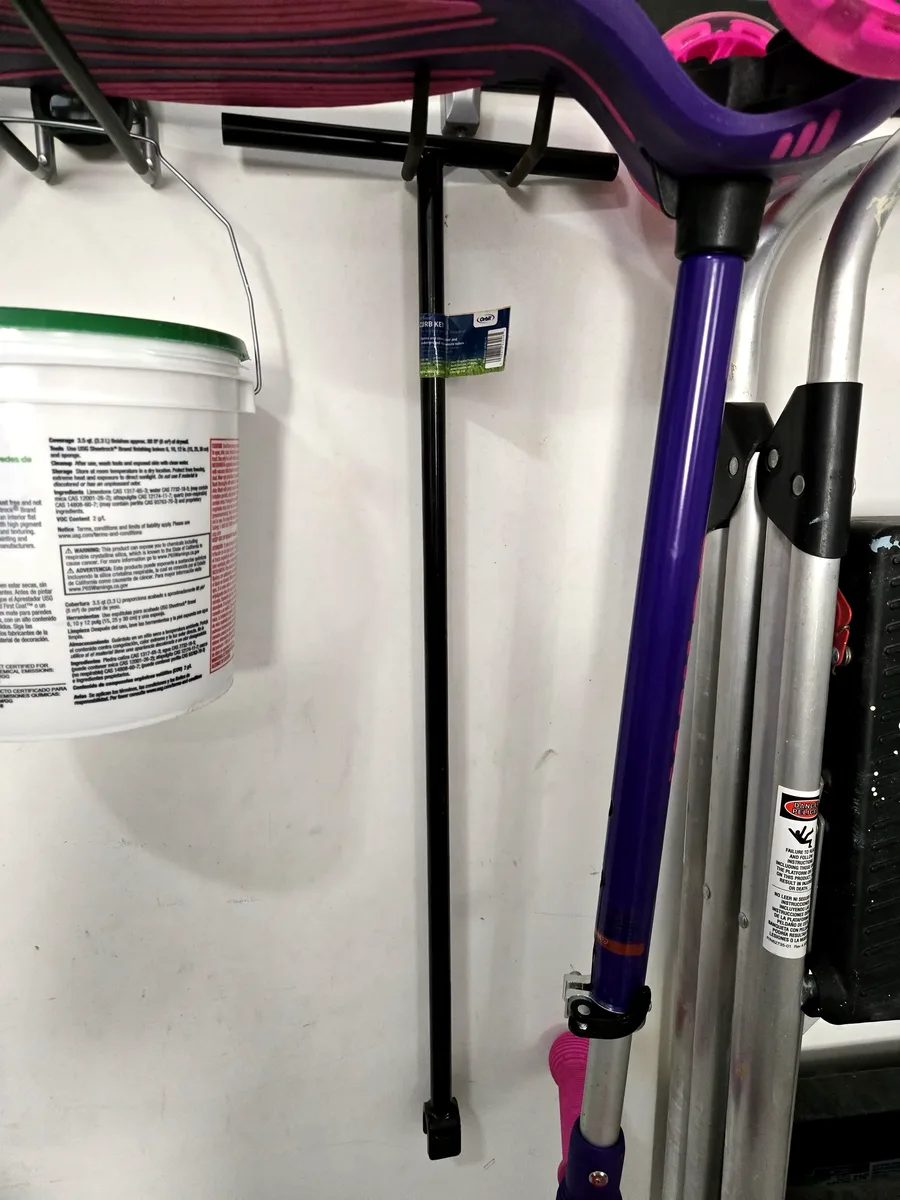 Water meter key (black T-handle) hanging on the FastTrack rail next to my daughter's scooter — always within reach