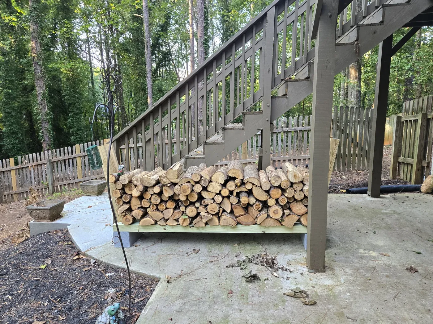 The firewood pile under the deck stairs — the trees that were too close to the house