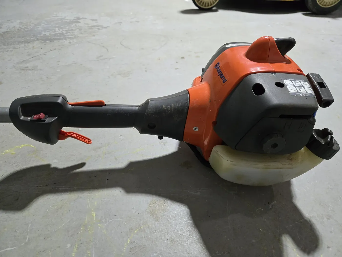 The Husqvarna trimmer — tank run dry, head due for fresh line, hung level on the wall for the winter