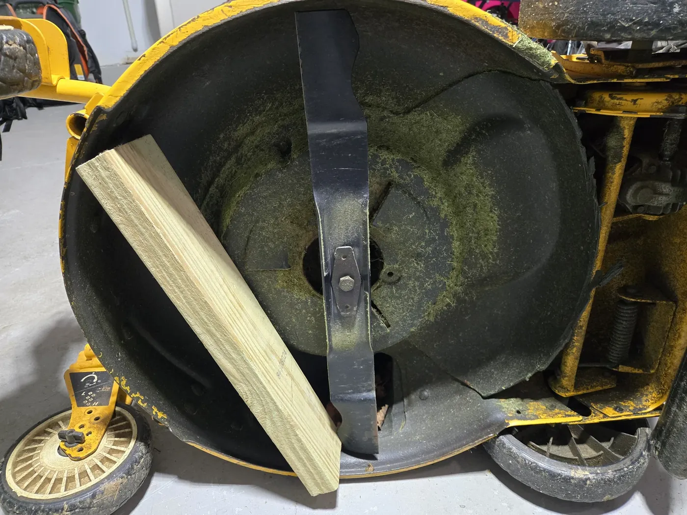 Underside of the mower deck with a 2x4 wedged between the blade and the deck