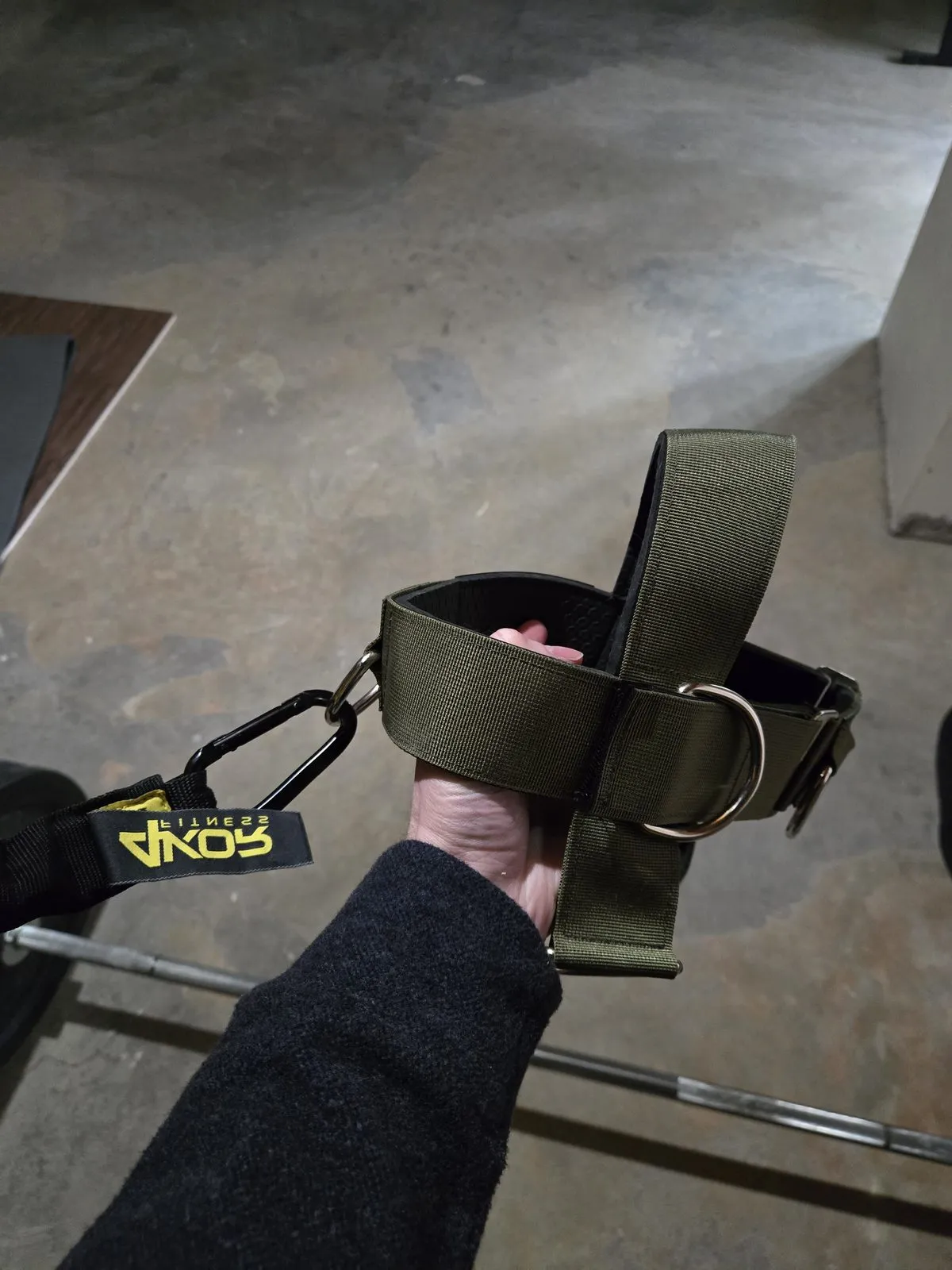 The Iron Neck Alpha Harness — olive green with a carabiner attachment point for connecting to resistance bands